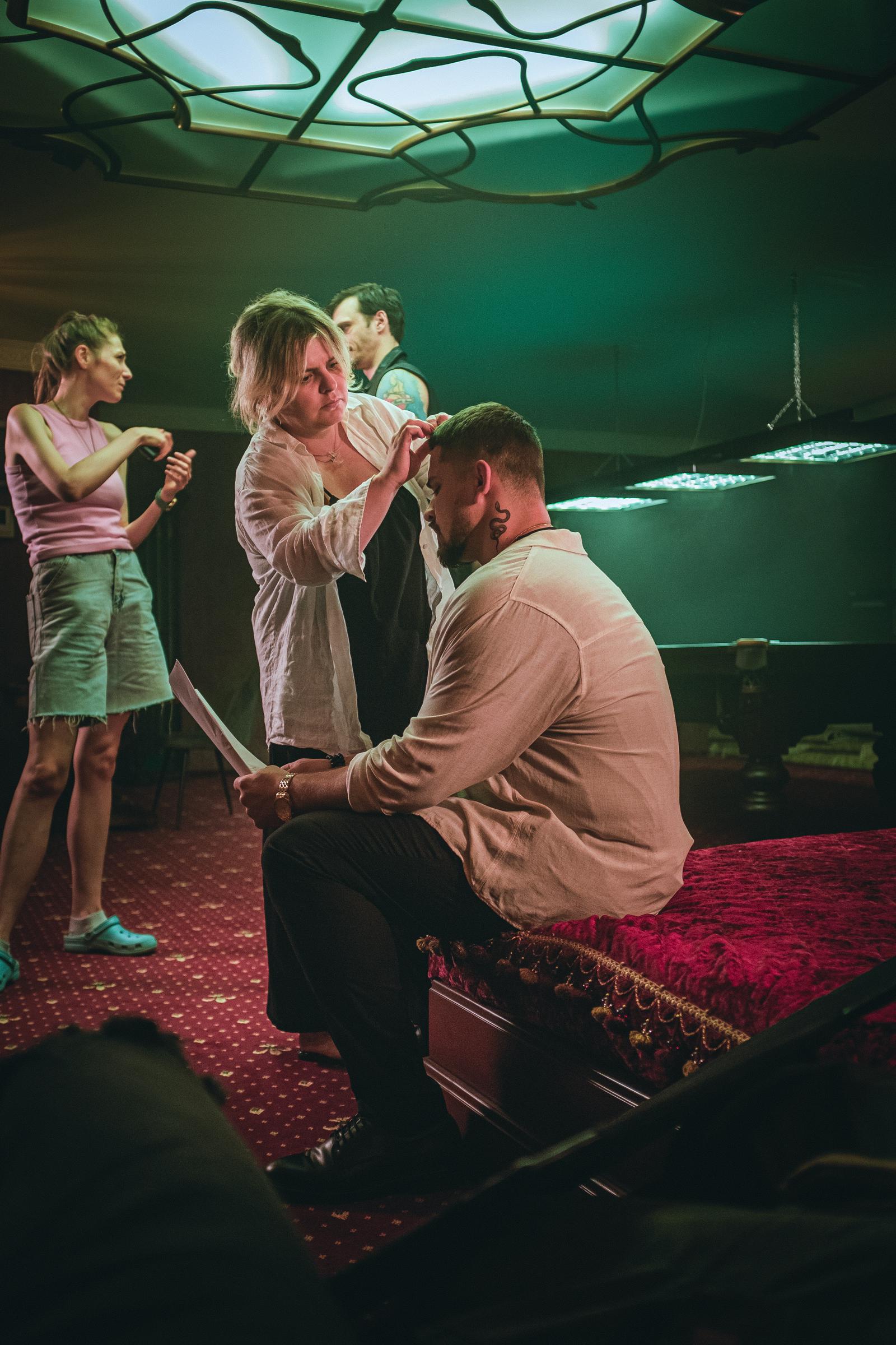 A makeup artist prepares Maksym Devizorov (Dante Crow) while director Alina Bukhtiyarova speaks with Anton Solovey (Luca Morelli) on the billiard room set. | Source: AMO Pictures