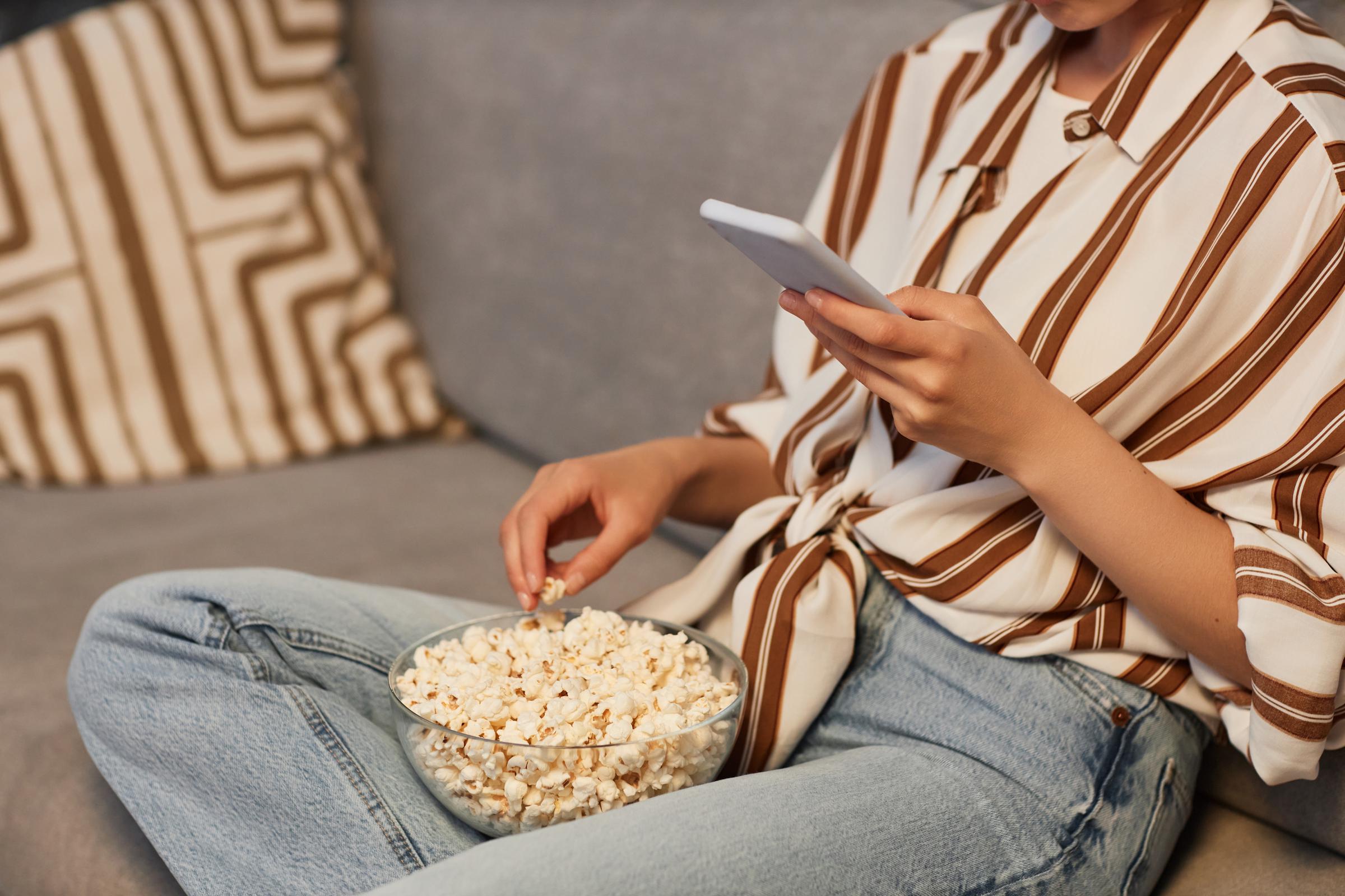 Person viewing her mobile phone while eating popcorn | Source: Shutterstock