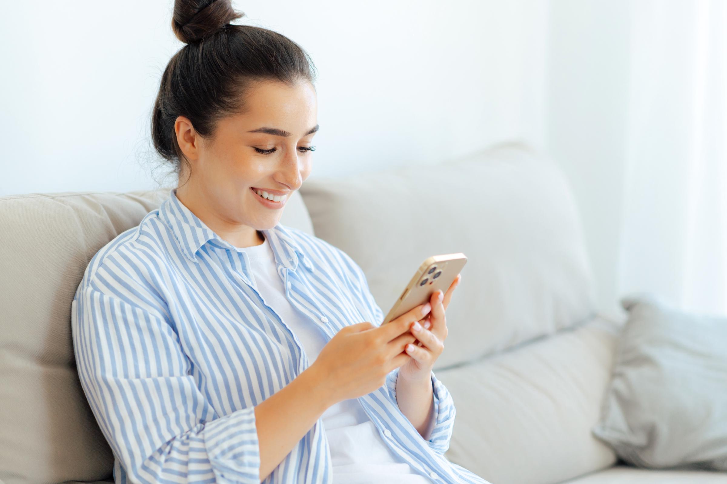 A woman smiling while viewing her phone | Source: Shutterstock